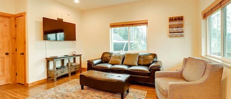 A living room with a leather sofa, a brown armchair, a wooden coffee table, and a large window with blinds.
