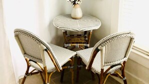 A corner room with two wicker chairs, a small round table with a vase, and two wall-mounted mirrors.