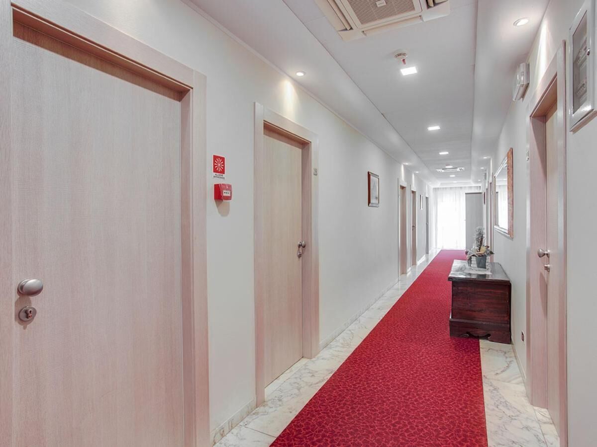 A hotel corridor with wooden doors, a red carpet, and a marble floor.