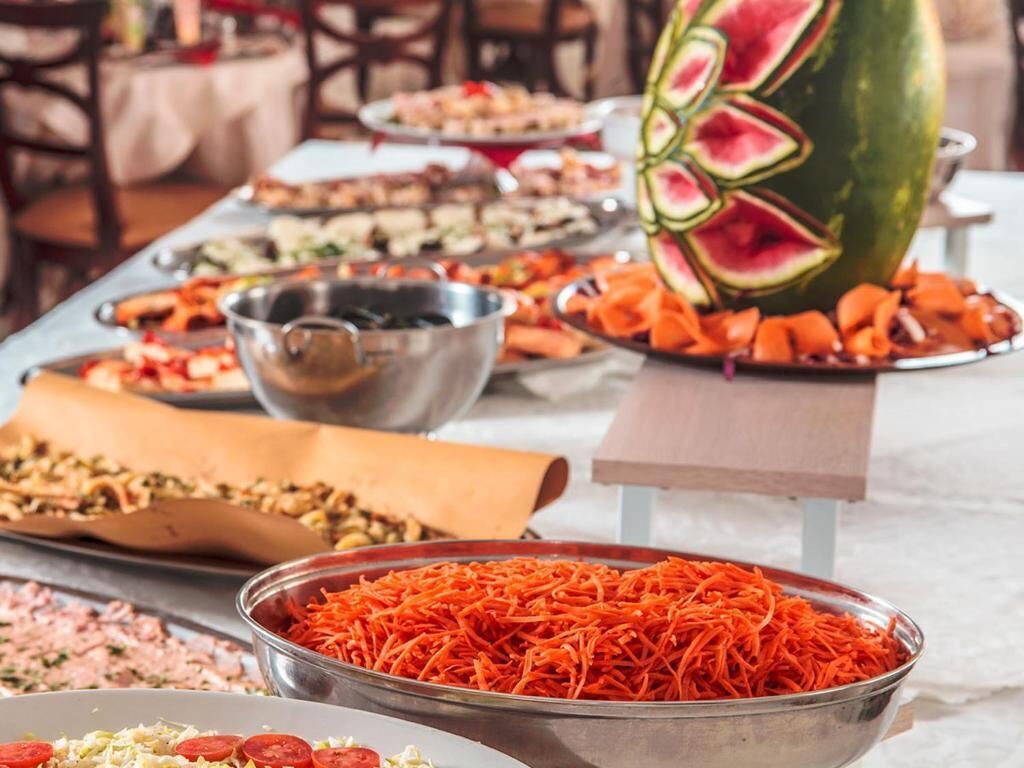 A buffet table with various food items, including sliced watermelon, shredded carrots, and other dishes.