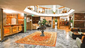 A hotel lobby with a marble floor, a central rug, seating areas, and a mezzanine level with a railing. - Hotel Caravelle (Cesenatico)