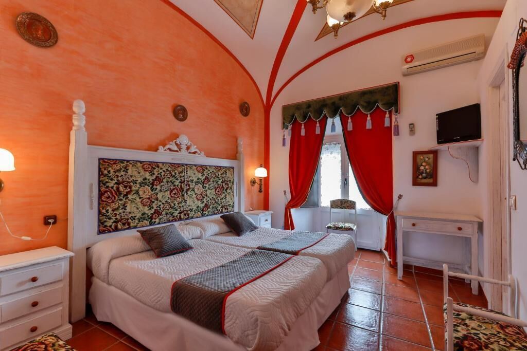 Habitació d'hotel amb dos llits, una tauleta de nit blanca, escriptori i cortina vermella.
