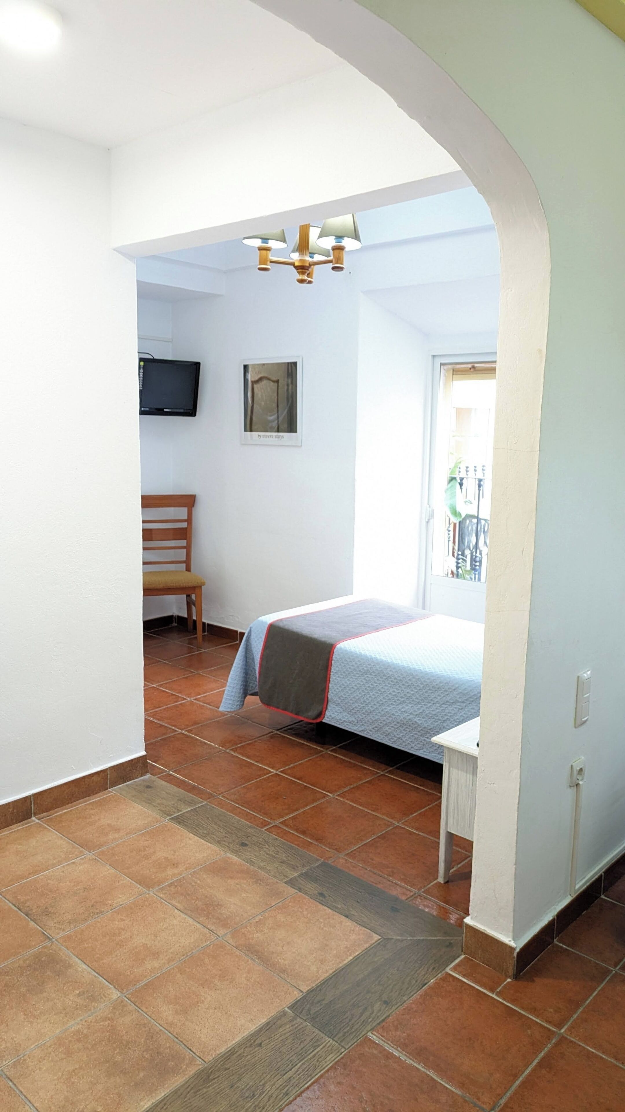 Un dormitorio con una cama, una silla, un televisor y una ventana.