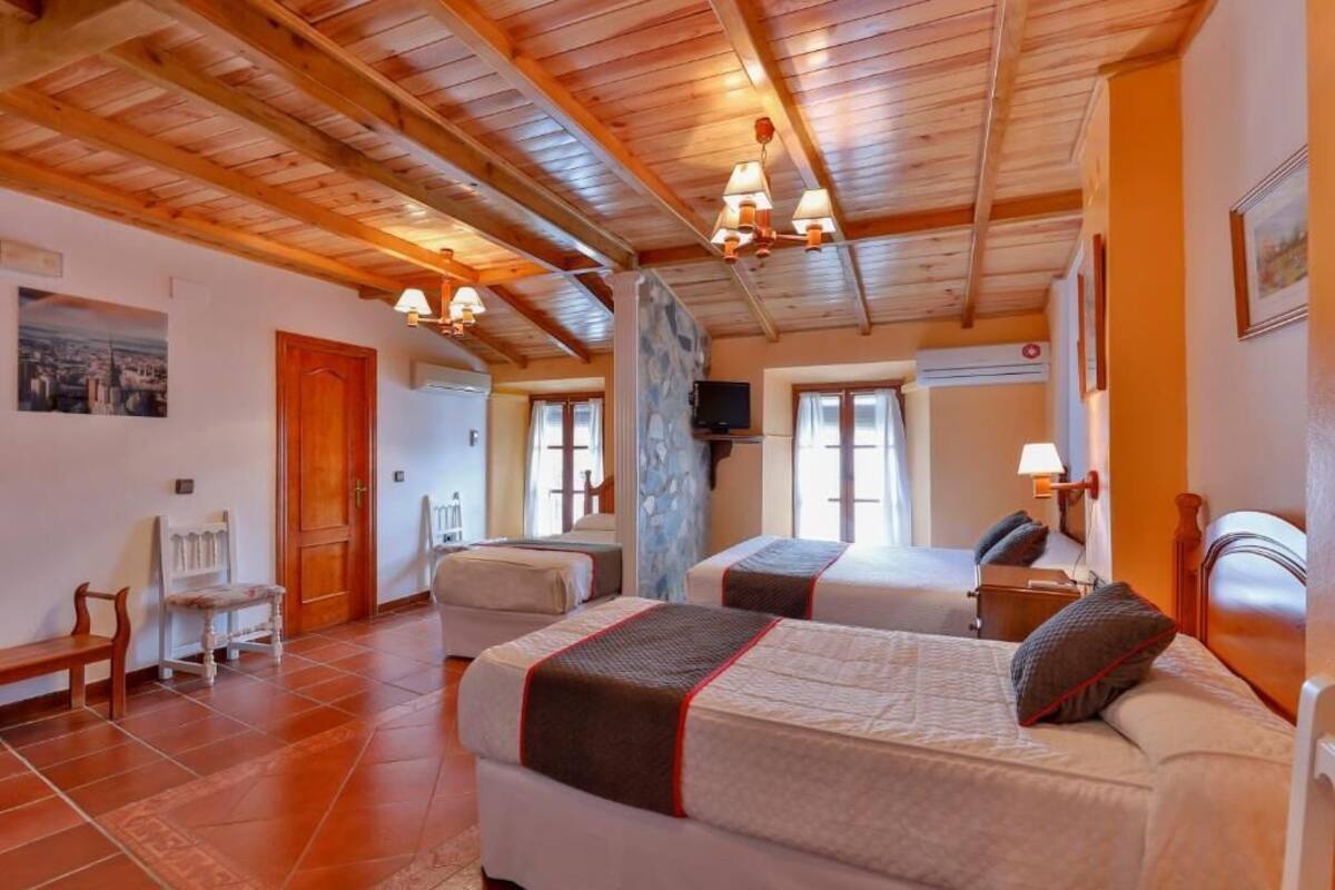 Habitación de hotel con dos camas, vigas de madera en el techo y piso de baldosas.