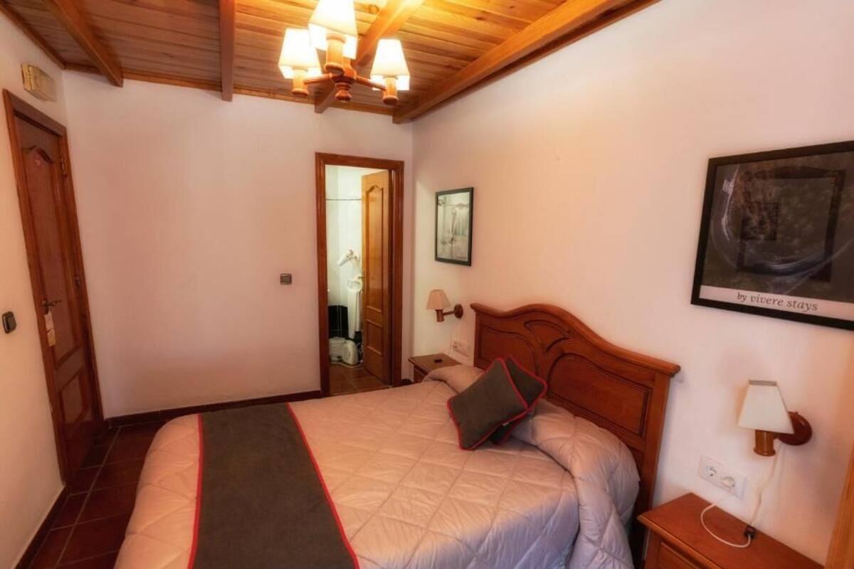 Un dormitorio con cama, cabecero de madera, lámpara de noche y una obra de arte enmarcada en la pared.