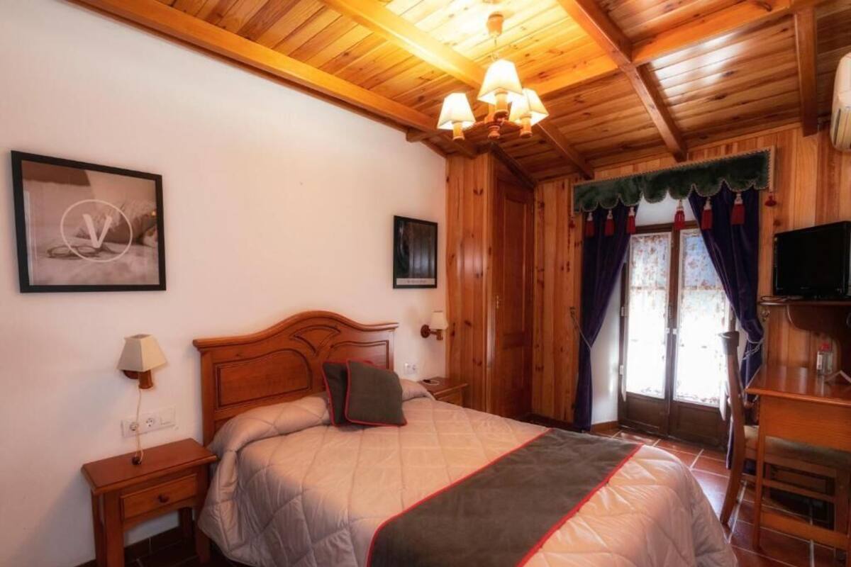 Un dormitorio con paneles de madera, una cama, mesita de noche, lámpara y televisor.