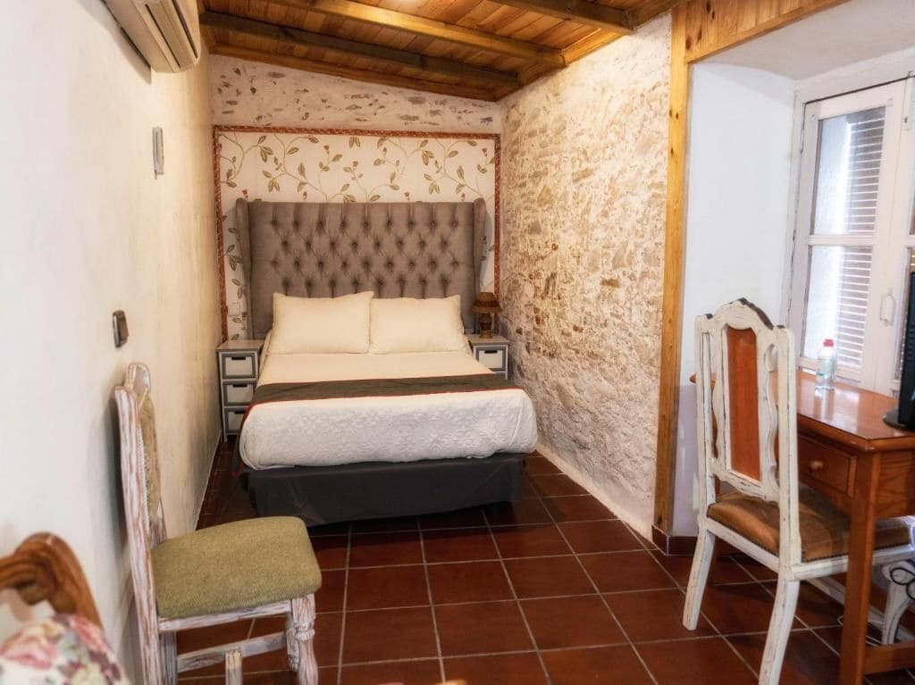Un dormitorio con una cama, una silla, un escritorio y una pared de piedra.