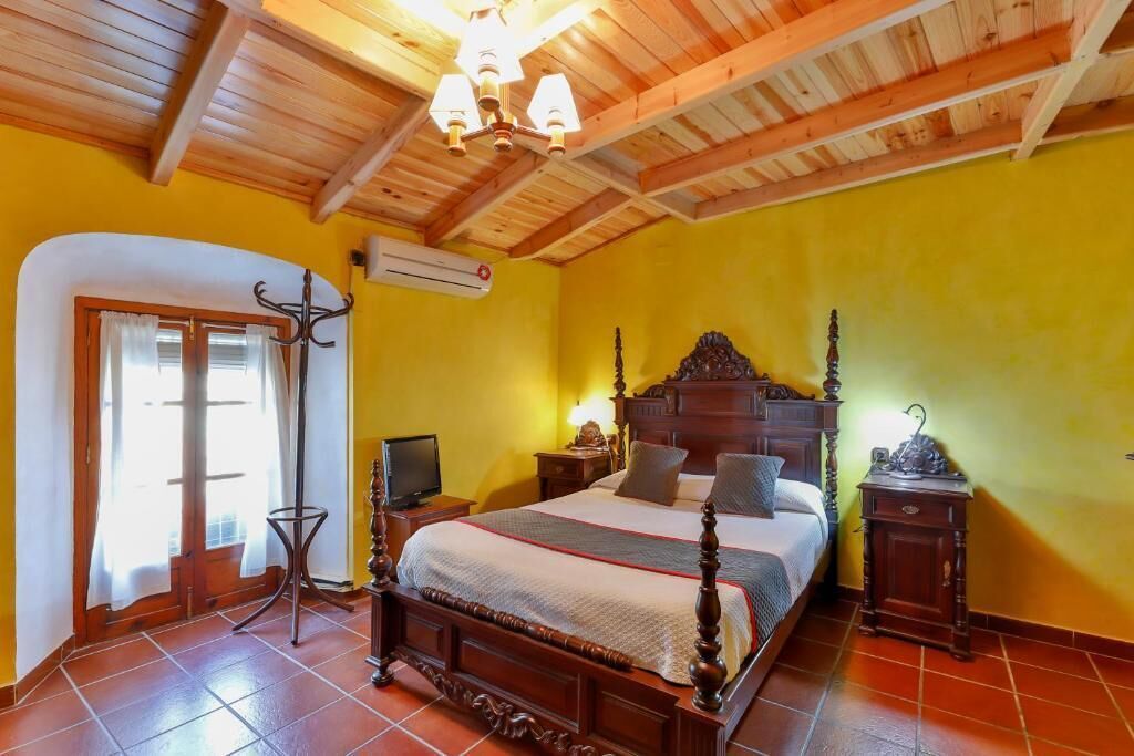 Un dormitorio con techo de madera, una cama con cabecera de madera, una mesita de noche, una lámpara y un armario.