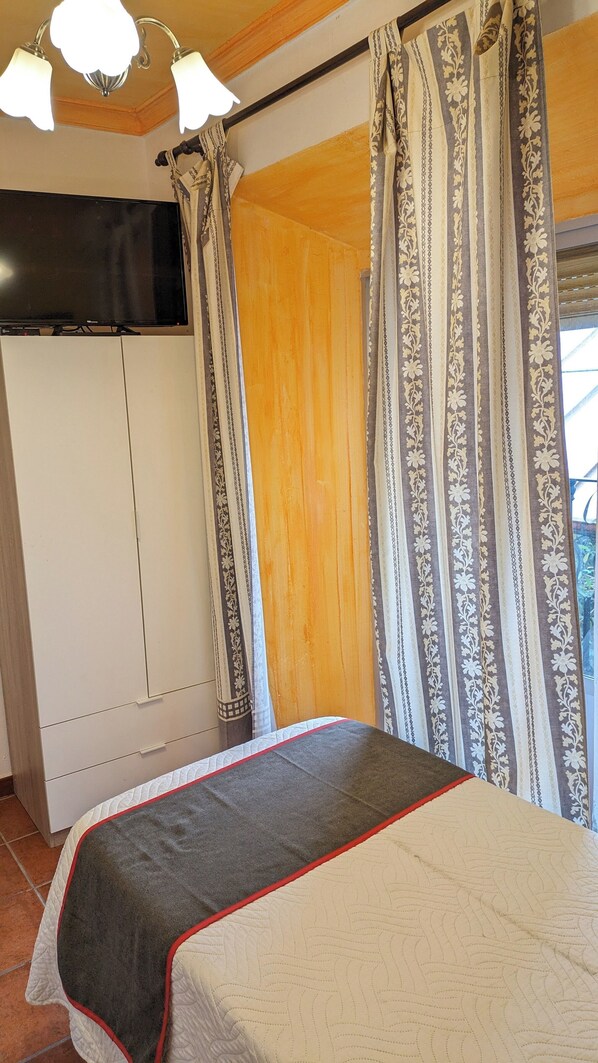 Une chambre à coucher avec un lit, des rideaux, une armoire et un téléviseur.