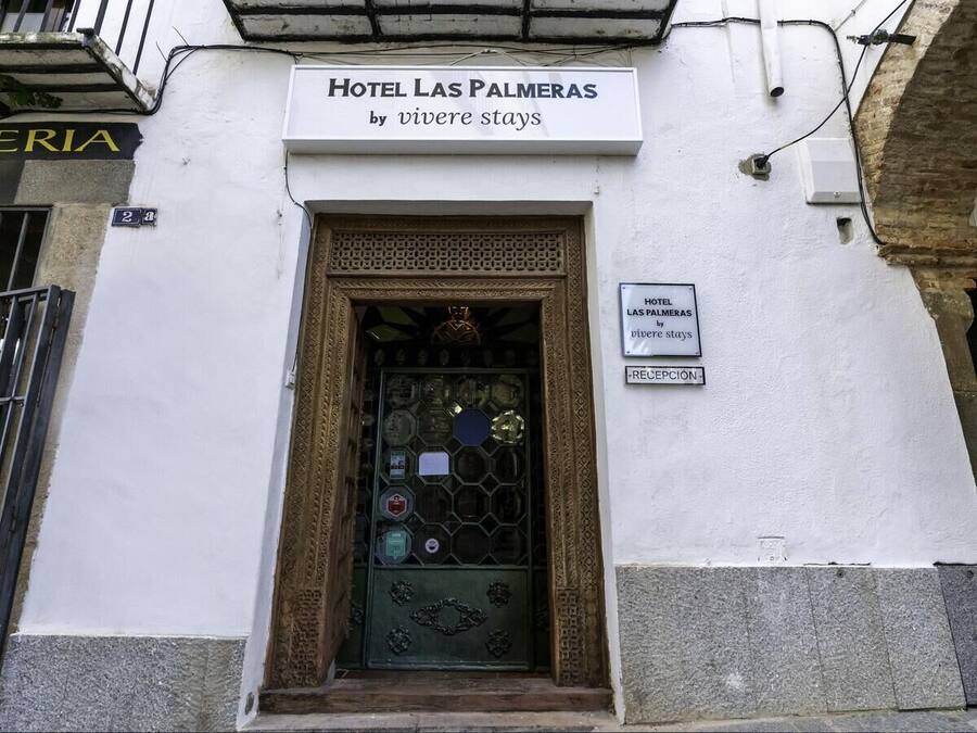 A hotel entrance with a sign reading "Hotel Las Palmeras by viveire stays" and a reception sign below.