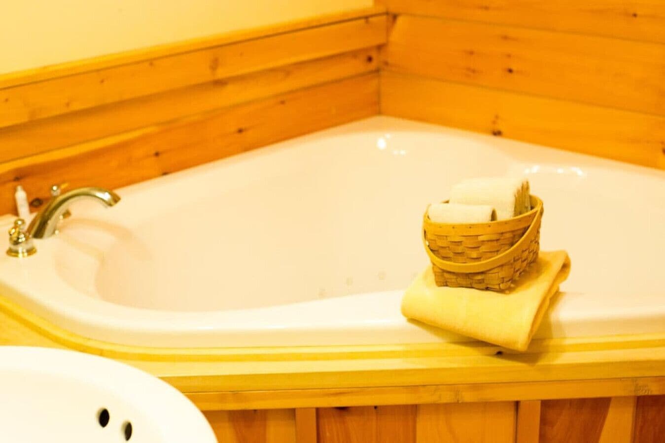 Une baignoire en bois avec un robinet et un panier rempli de serviettes.