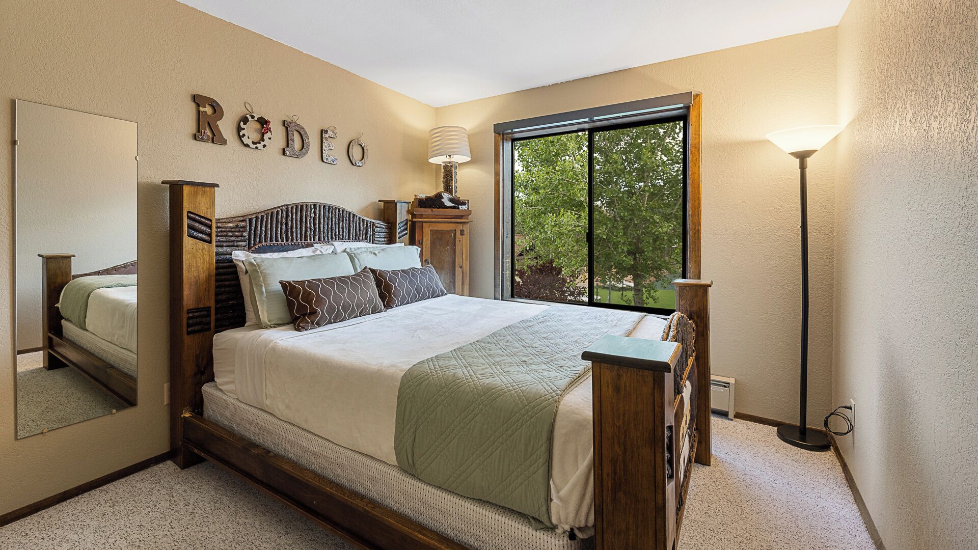 A bedroom with a bed, a mirror, a window, and a lamp.
