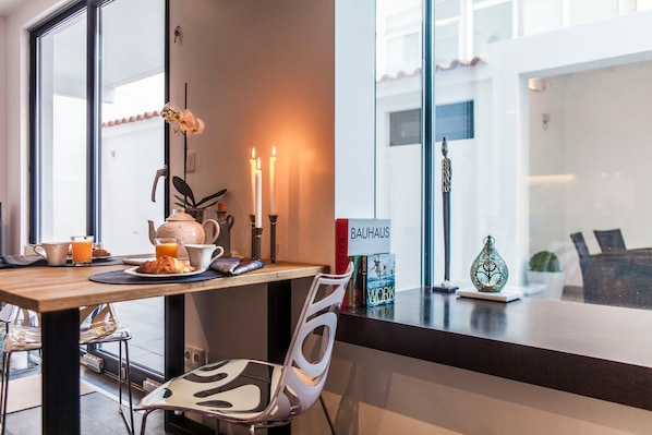 A modern dining area with a wooden table, a white chair, and a view of the outside through large windows.