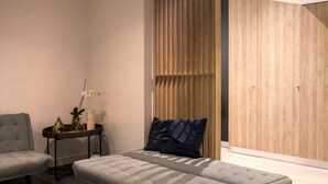 Een moderne slaapkamer met een bed, een stoel, een klein tafeltje met een vaas en een plant, en een houten garderobe.