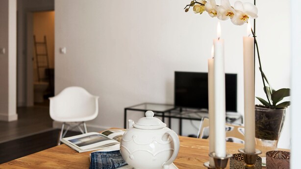 Een houten tafel met een witte theepot, twee kaarsen en een orchidee.