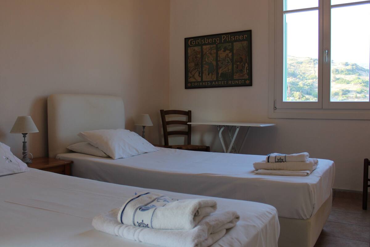 Habitación de hotel con dos camas, una silla, una mesa y ventana con vistas.