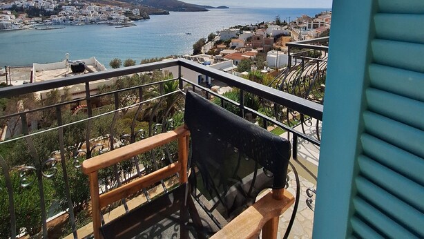 A balcony with a view of a coastal town, a chair, and a railing. - Blue Dolphin (Andros)