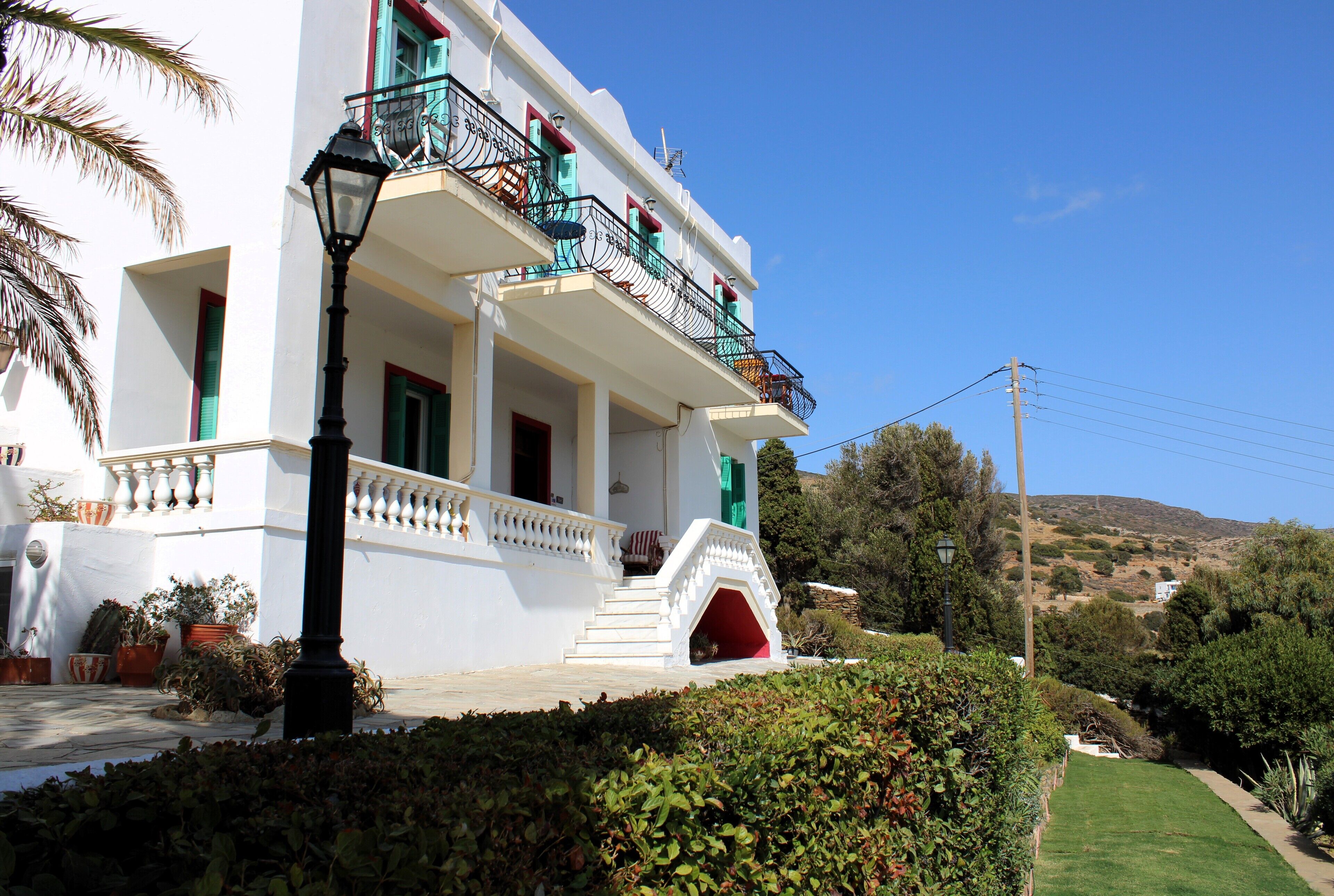 Um edifício branco com varandas, uma porta vermelha e um jardim bem cuidado.