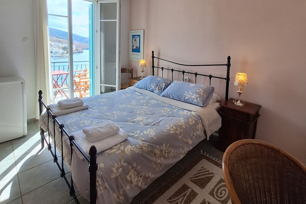 Un dormitorio con una cama, una silla, una mesita de noche, una lámpara, una ventana y una puerta.