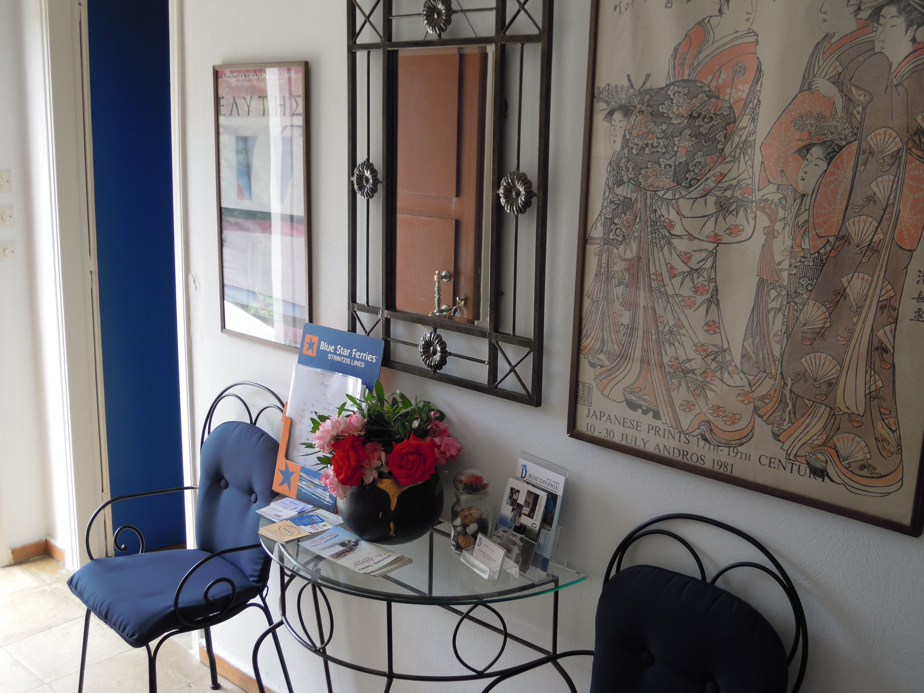 Un área de recepción con una mesa de vidrio, sillas azules, un florero con flores, una impresión japonesa enmarco y un letrero de Blue Star Ferries.