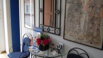 Un área de recepción con una mesa de vidrio, sillas azules, un florero con flores, una impresión japonesa enmarco y un letrero de Blue Star Ferries.