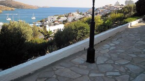 A stone-paved pathway with a black lamppost, overlooking a coastal town with white buildings and sailboats on the water. - Blue Dolphin (Andros)