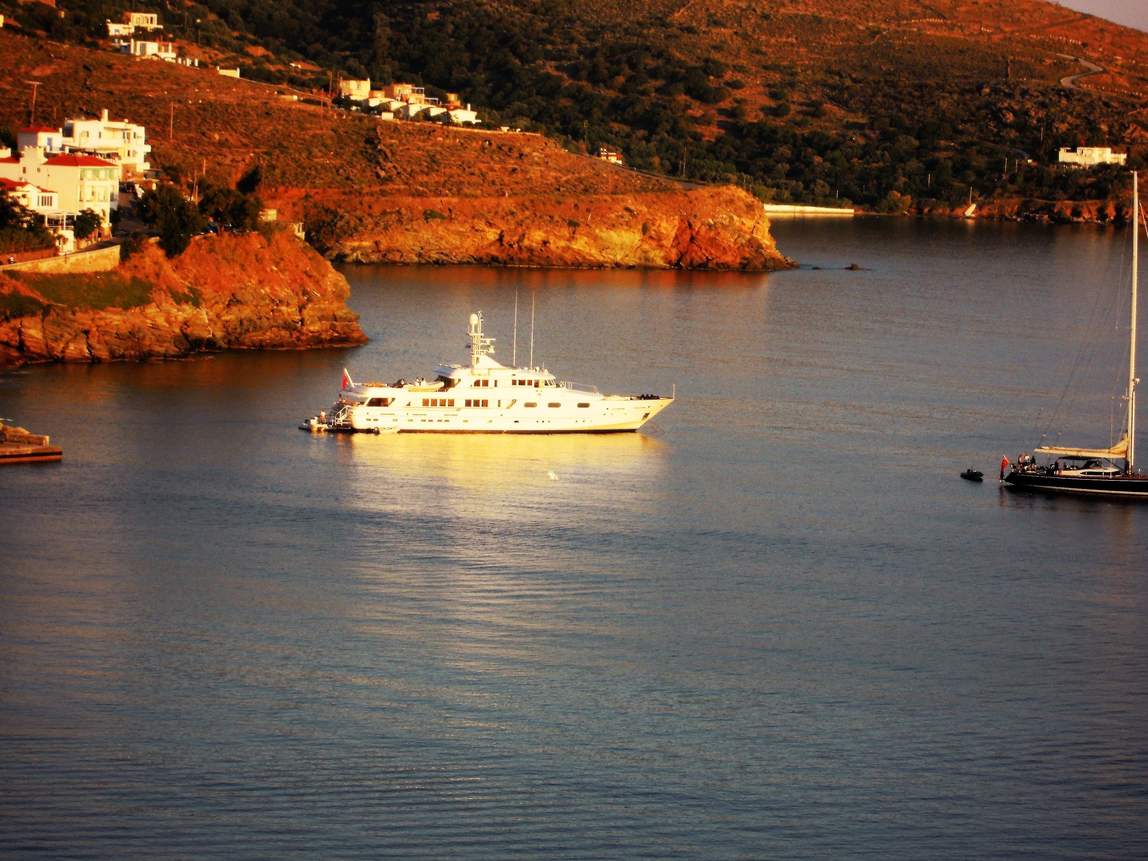 Un grand yacht est amarré dans une baie tranquille, avec un paysage vallonné en arrière-plan.