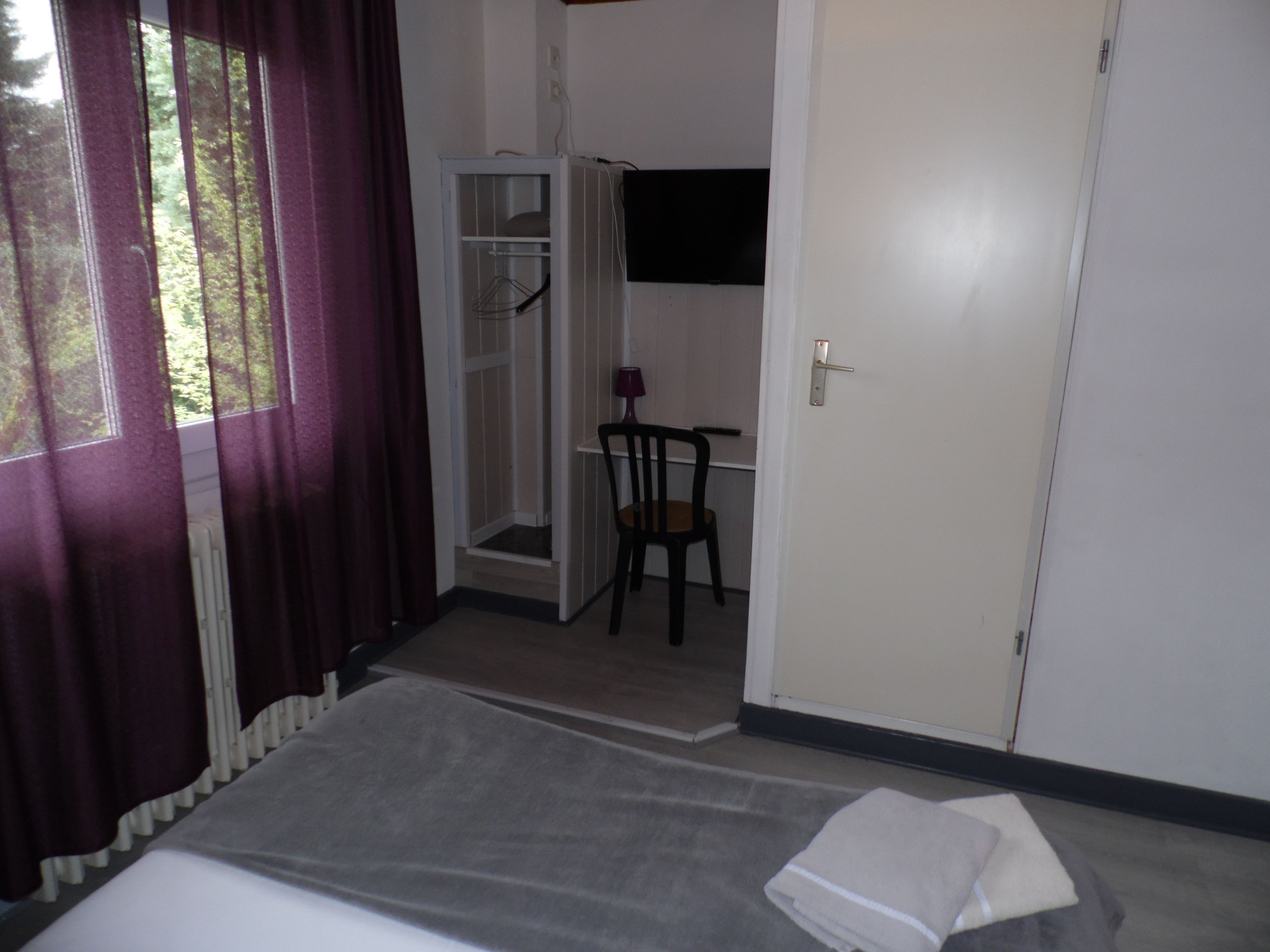 Una habitación de hotel con cama, una silla, armario y ventana con cortinas.