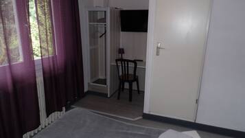 Una habitación de hotel con cama, una silla, armario y ventana con cortinas.