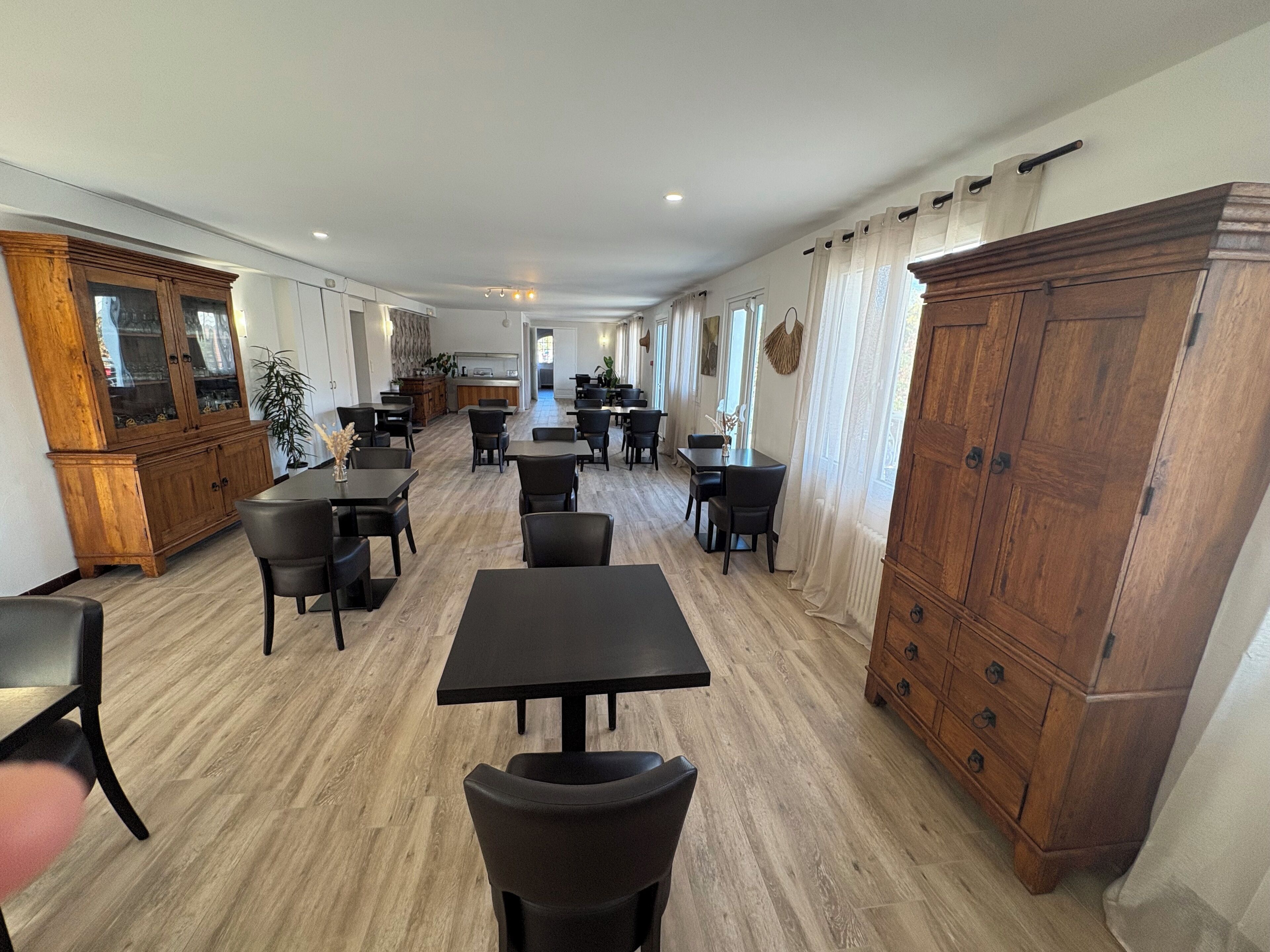 A spacious dining area with multiple tables and chairs, wooden cabinets, and a kitchen in the background.