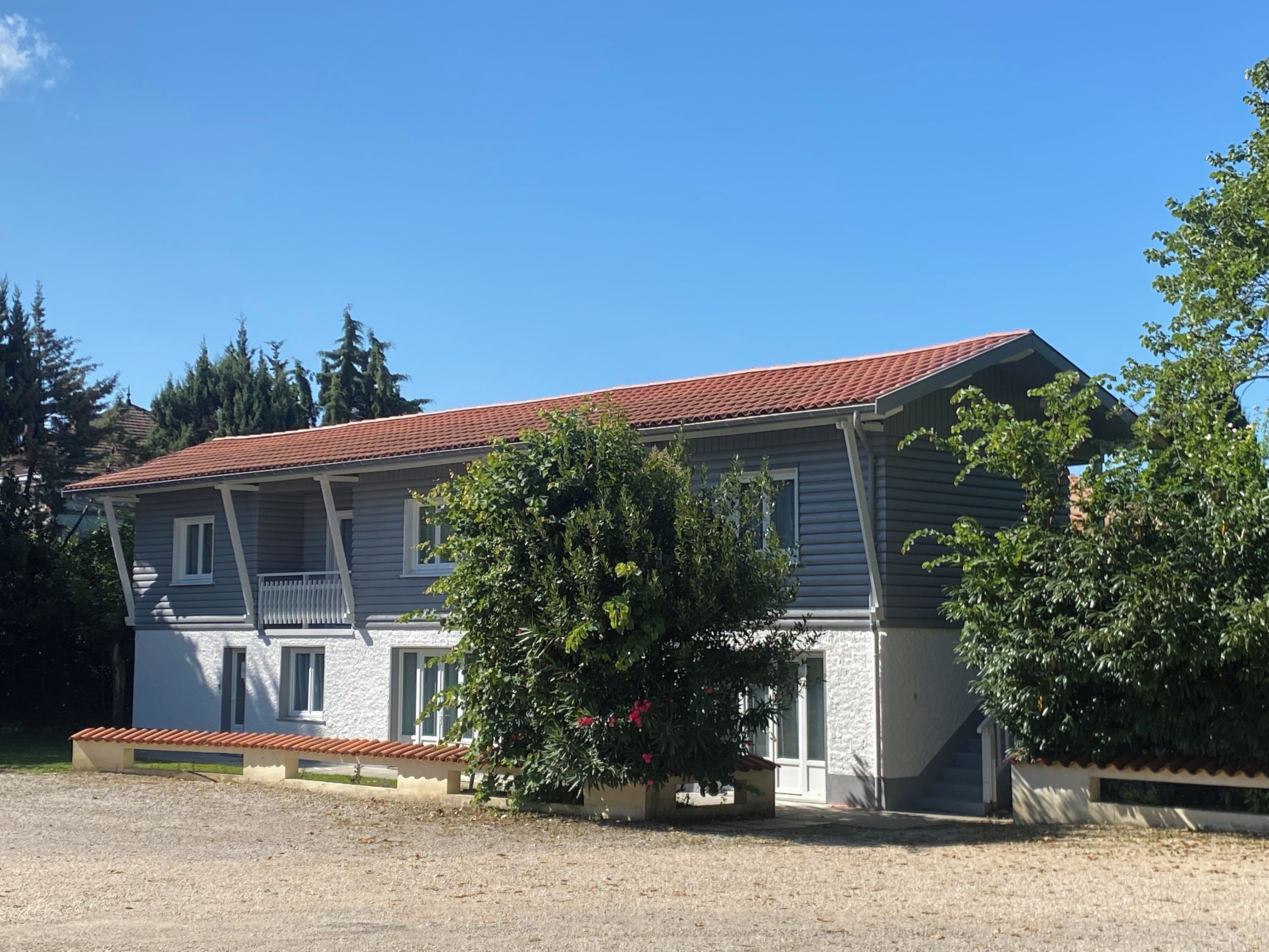 A two-story house with a red-tiled roof, a balcony, and a front porch.
