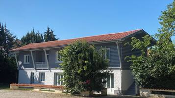 Een huis met twee verdiepingen, een rode dakbedekking van tegels, een balkon en een voortuin.