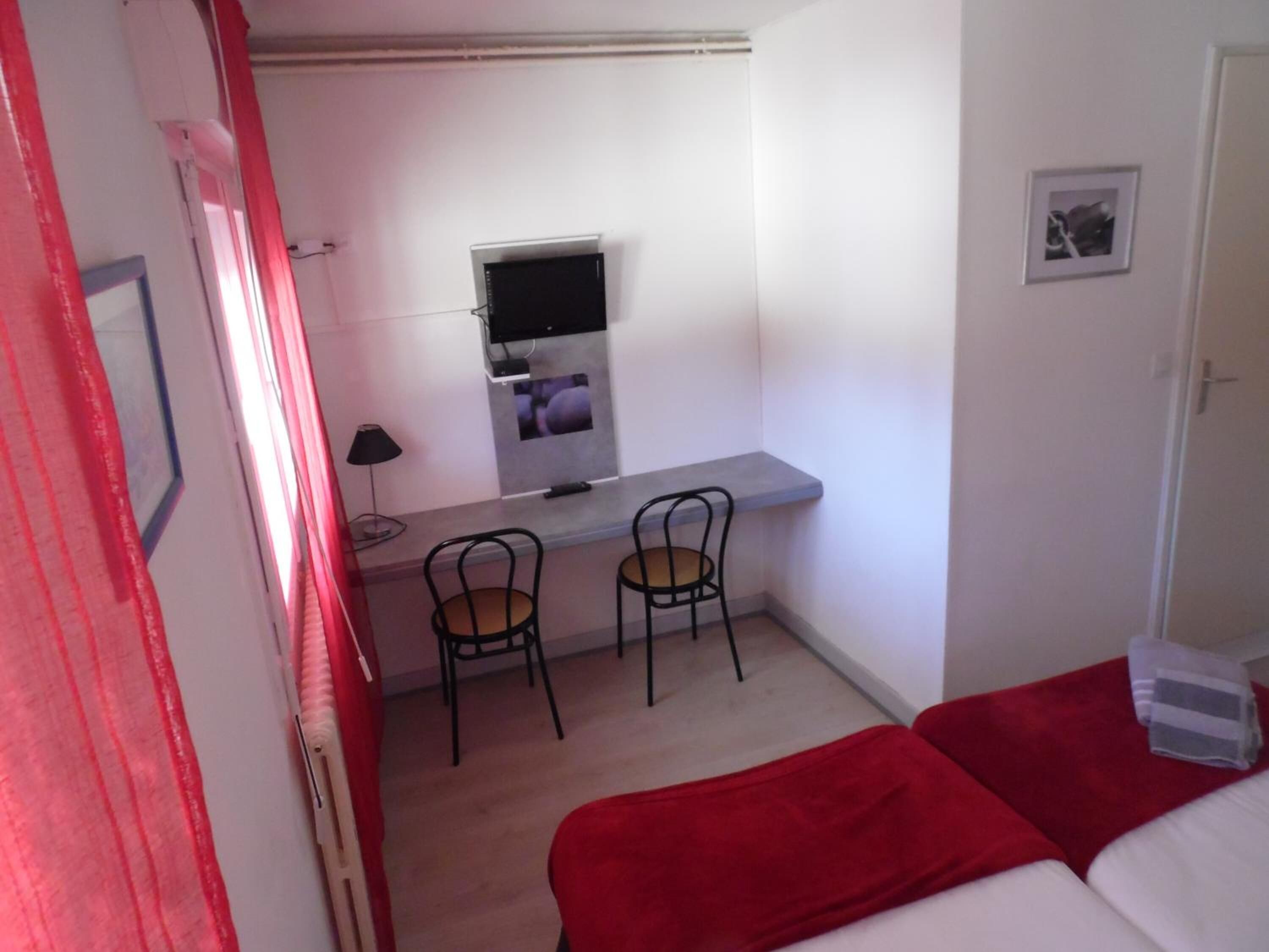 Une petite pièce, de taille modeste, comprenant un lit, un bureau avec deux chaises, une télévision et une petite fenêtre.