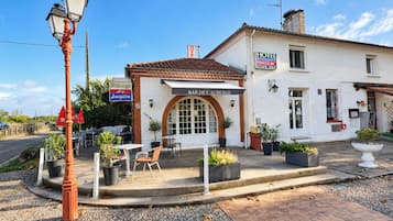 Un hôtel à la façade blanche, doté d’un espace extérieur couvert avec des sièges et d’un panneau indiquant la disponibilité de places de stationnement.