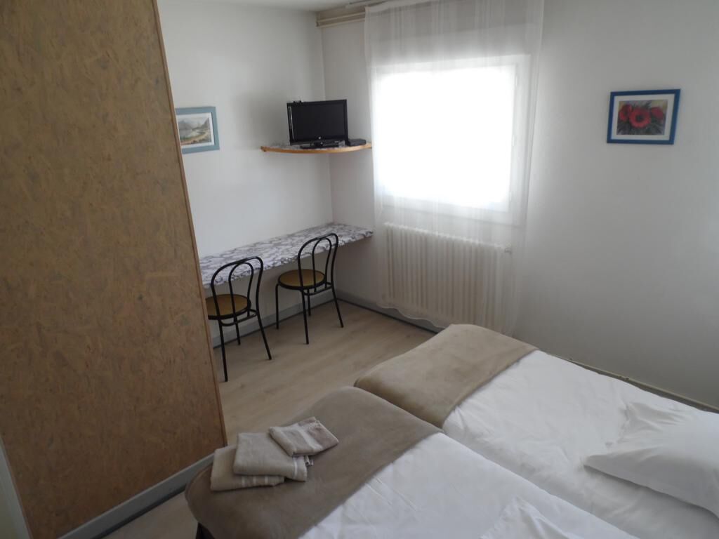 Een slaapkamer met twee bedden, een bureau met stoel, een televisie en een raam met dunne gordijnen.