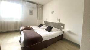 Een hotelkamer met twee bedden, een radiator, een airconditioner en een raam met dunne gordijnen.