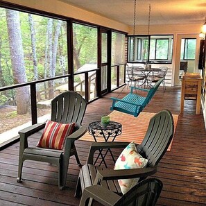 Un portico coperto con poltrone Adirondack, un tavolo e vista su una foresta.