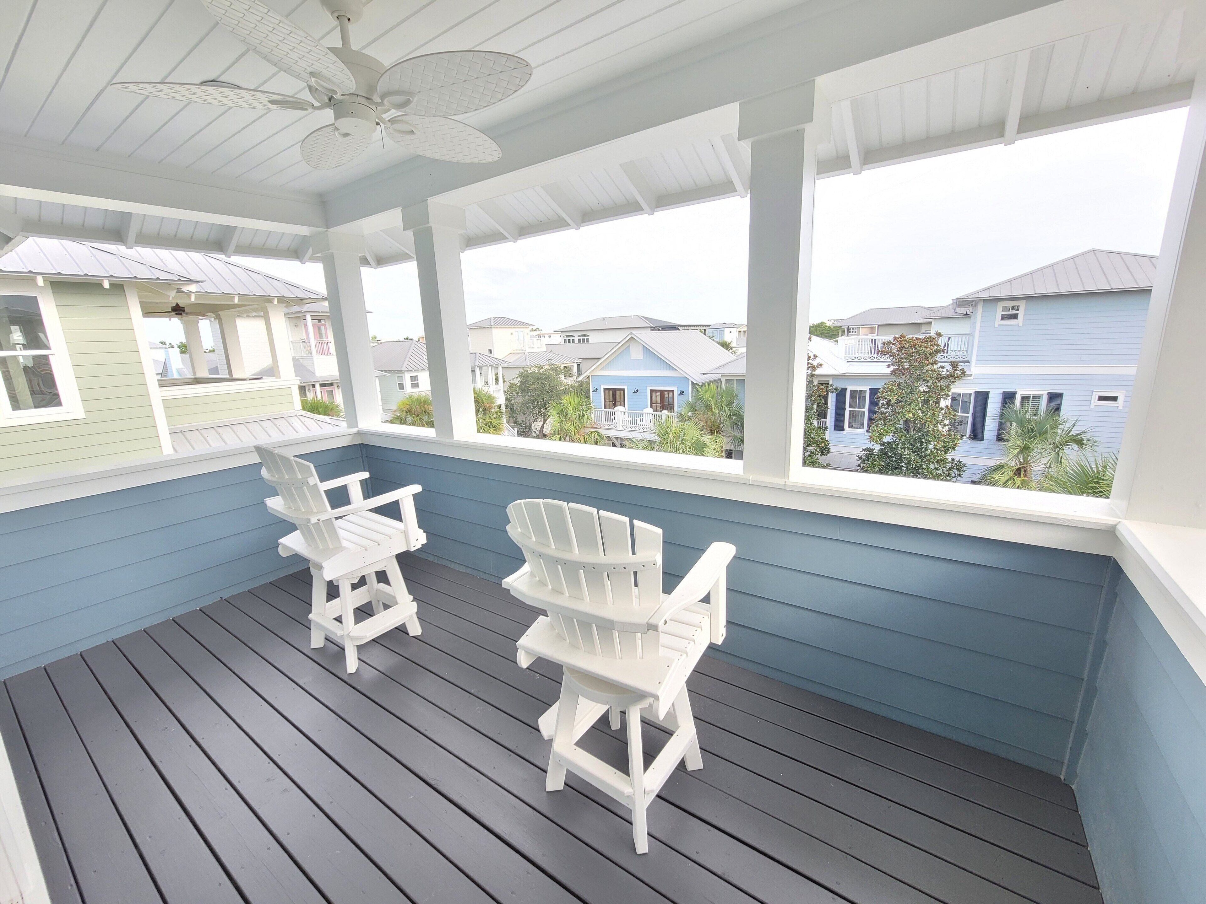 Eine überdachte Veranda mit zwei Adirondack-Stühlen, einem Deckenventilator und Blick auf Nachbarhäuser.