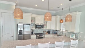 Una cocina moderna con armarios blancos, encimera de granito y tres taburetes blancos.