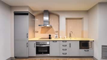 A modern kitchen with grey cabinetry, a stainless steel range hood, a built-in oven, a microwave, and a yellow countertop.