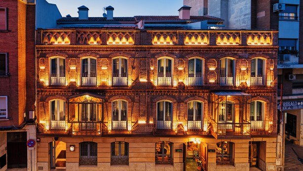 Un edificio de dos pisos con múltiples ventanas y balcones, con fachada de ladrillo y detallada rejería.