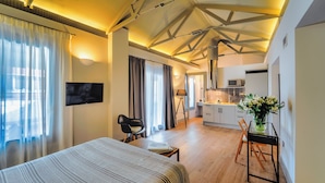 Una habitación de hotel moderna con cama, escritorio, silla, televisor, zona de cocina y mesa de comedor con sillas.