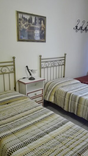 A bedroom with two beds, a nightstand, a desk with a lamp, and a painting on the wall. - B&B Candido Vacanze (Modica)