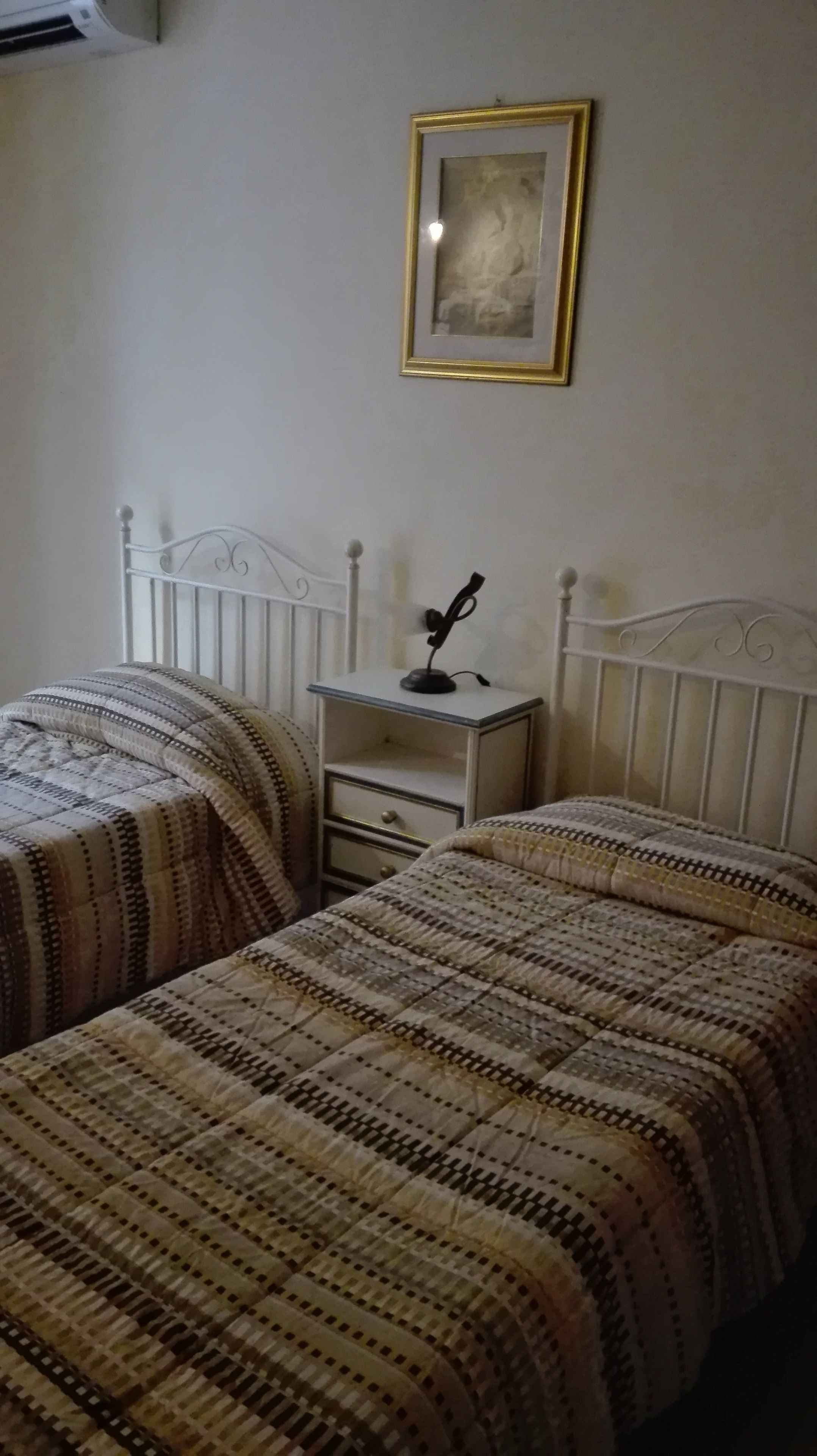 Quarto com duas camas, mesa de cabeceira com abajur e quadro na parede.