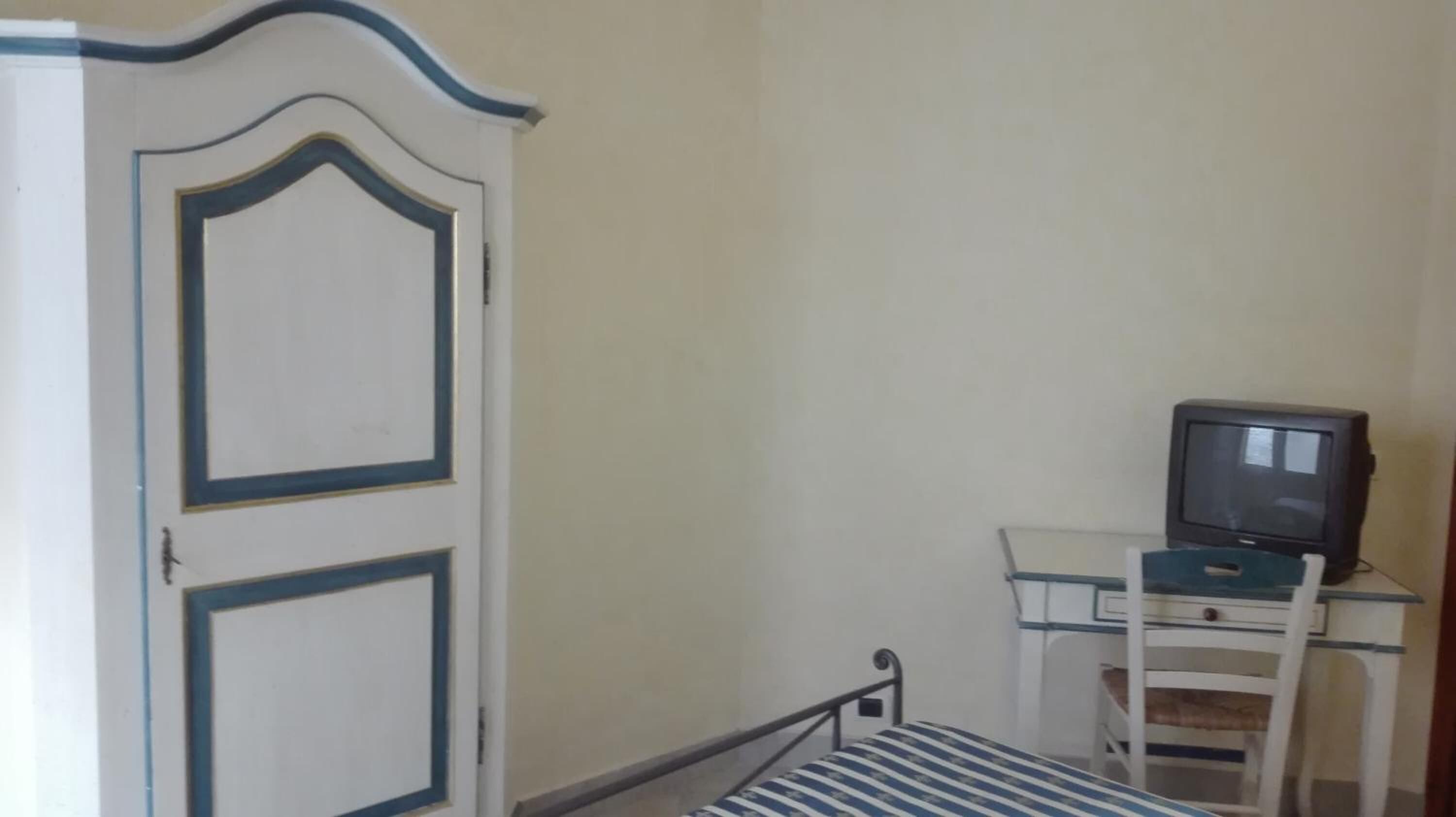 A room with a bed, a desk with a television, and a door with decorative moldings.