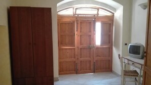 Una habitación con puerta de madera, un televisor sobre un mueble bajo y una silla.