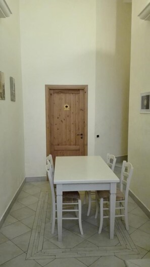 A dining area with a white table and chairs, a wooden door, and tiled flooring. - B&B Candido Vacanze (Modica)