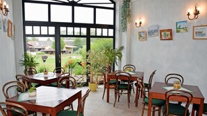 A dining area with wooden tables and chairs, potted plants, and artwork on the walls.