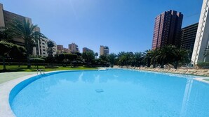 Une grande piscine vide, à bords incurvés, entourée d’une zone pavée et de palmiers.