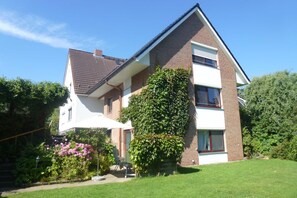 A two-story house with a brick facade, a tiled roof, and a garden with pink flowers and a chair.